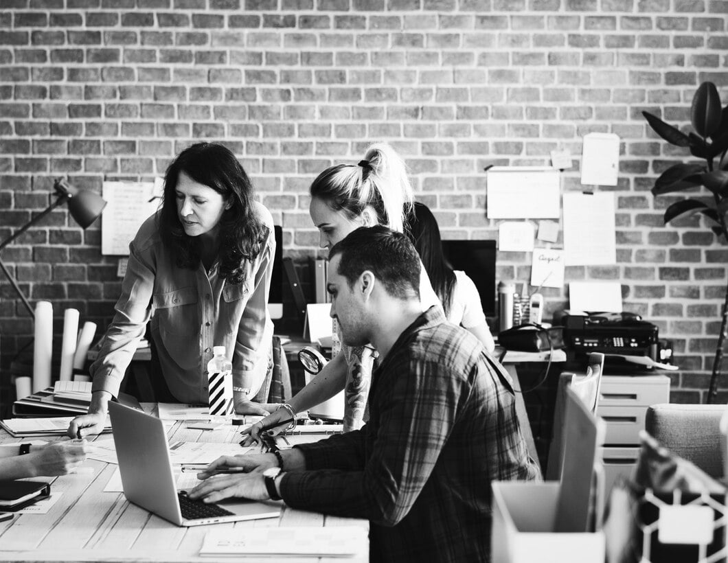 2 women and a man sitting at a desk in front of a laptop and documents